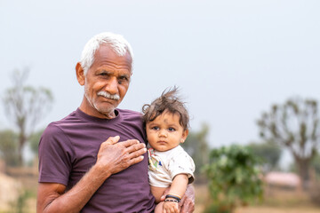 Elderly indian man holding a baby outdoors