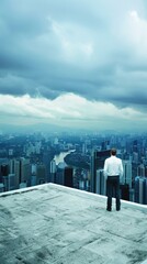 Obraz premium A man in a white shirt and black pants stands on a cliff, gazing out at a city river. The cityscape is visible in the distance, with tall buildings and a cloudy sky