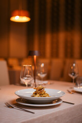 Piatto di rigatoni con carciofi fritti croccanti, fiori di zucca e pancetta croccante servito come primo piatto in un ristorante elegante