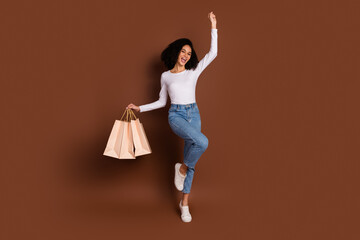 Full size photo of pretty young girl raise fists hold bags wear pullover isolated on brown color...
