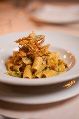 Piatto di rigatoni con carciofi fritti croccanti, fiori di zucca e pancetta croccante servito come primo piatto in un ristorante elegante