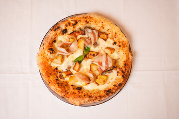 Pizza tradizionale napoletana con mozzarella, pancetta affumicata, patate al forno e basilico fresco servita in una pizzeria