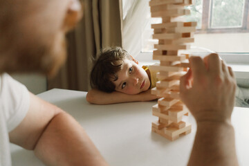 A father and son play a block tower game together indoors. The game is taking place on a white table, and the background is out of focus. Father's day © Анастасія Стягайло