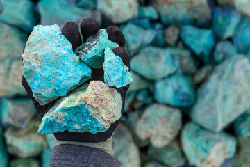 Blue green copper (Cu) oxide ore, held in hand with protective glove, against background of ore that is out of focus. Mining.