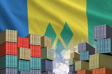 Saint Vincent and the Grenadines flag and big stack of shipping cargo containers in docks with sky...
