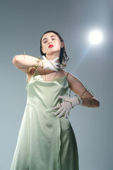 Fototapeta premium A beautiful young woman with red lips poses in a green dress and white gloves in a studio setting against a grey backdrop.