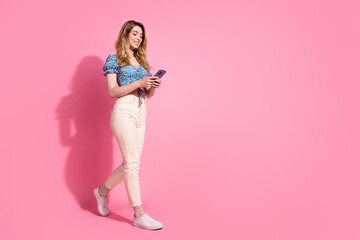 Full length photo of lovely young lady hold device walking dressed blue flower print garment isolated on pink color background