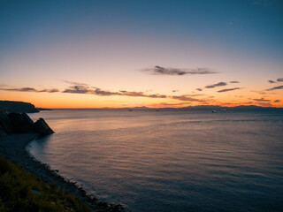 Sunset over rocky beach with silhouetted cliffs and calm ocean waters