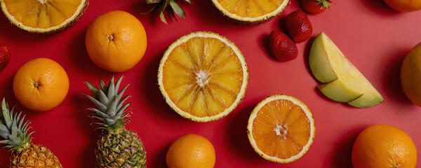 A variety of fresh fruits, including oranges, pineapple, and mango, arranged on a red background