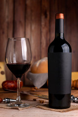 glass of red wine with wine bottle with cheese board country bread wooden board fresh grapes knife and cork opener and bottle