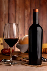 glass of red wine with wine bottle with cheese board country bread wooden board fresh grapes knife and cork opener and bottle