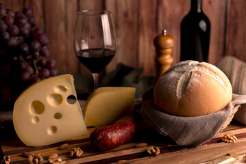 glass of red wine with wine bottle with cheese board country bread wooden board fresh grapes knife...