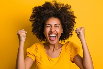 Black woman with fist celebrating promotion or lottery bonus on yellow background. Happy model, deal, or lottery winner in studio