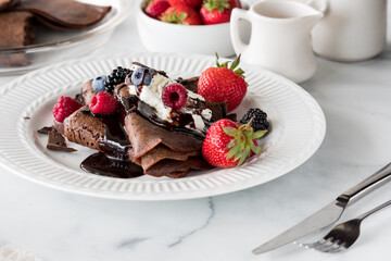 Chocolate crepes topped with whipped cream, berries and chocolate sauce.