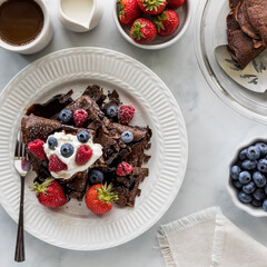 Chocolate crepes topped with whipped cream and berries, ready for eating.