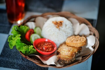 Fried chicken rice and tempeh with mustard greens and chili sauce on a rattan plate, ready to eat
