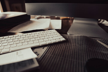 Desk with computer, keyboard, sheets, documents at the end of a difficult day at work.