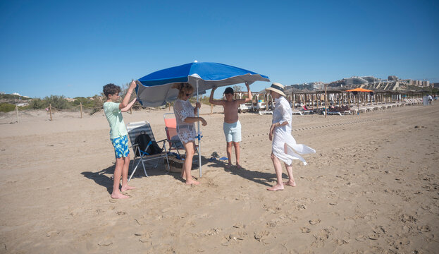 Three-generation family setting up beach umbrella on sunny day