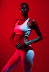 Fototapeta premium Red light, black woman and sportswear in studio with confidence for fitness, workout and exercise. Female person, portrait and serious on bodybuilding with training for body health and wellness