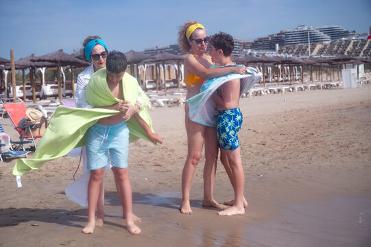 Grandmother and mother drying children with towels at the beach - Powered by Adobe