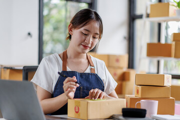 Portrait business woman smile and use laptop checking information on parcel shipping box before send to customer. Entrepreneur small business working at home. SME business online marketing.