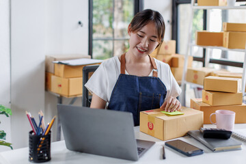 Portrait business woman smile and use laptop checking information on parcel shipping box before send to customer. Entrepreneur small business working at home. SME business online marketing.