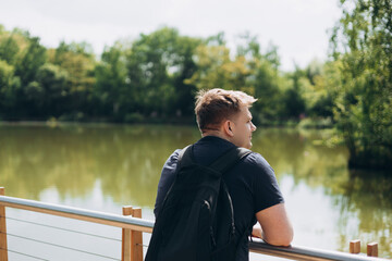 Fototapeta premium Sad man standing on wooden pier. Thinking about life. Peaceful atmosphere in sunny morning. Spending time alone in nature. Summer time, travel and rest banner