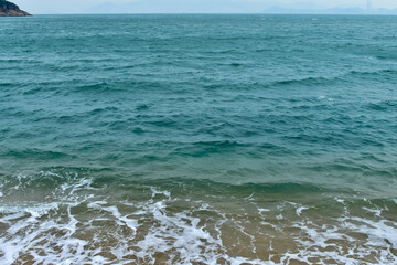Close-up of soft waves sand beach and blue sea. Texture of water, white foam waves. Seascape, Sea background, Sea water with copy space, summer vacation concept. 