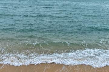 Close-up of soft waves sand beach and blue sea. Texture of water, white foam waves. Seascape, Sea background, Sea water with copy space, summer vacation concept. 