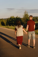 couple walking on empty road, young caucasian man and woman hold each other hands, warm summer evening, bright dawn, long shadows from low sun, love and family concept, vertical photo
