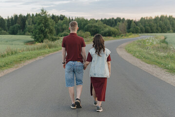 couple walking on empty road, young caucasian man and woman hold each other hands, warm summer evening, dawn, love and family concept