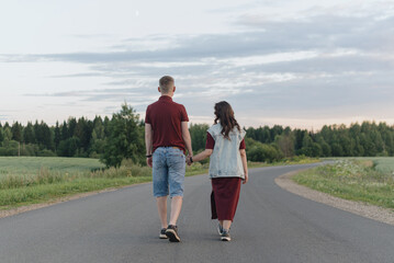 couple walking on empty road, young caucasian man and woman hold each other hands, warm summer evening, dawn, love and family concept