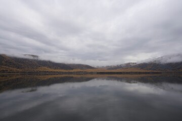 A serene landscape of a foggy surrounded by mountains with autumn foliage under a cloudy sky