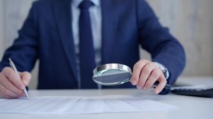 Businessman is carefully examining financial documents with a magnifying glass, highlighting the importance of thorough analysis in business. Audit and taxes