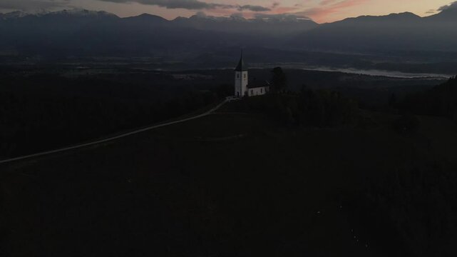 Aerial view of St. Primoz church at sunrise with Julian Alps peaks, Jamnik, Slovenia.