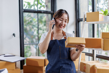 Starting small businesses SME owners asian female entrepreneurs call phone on receipt box and check online orders to prepare to pack the boxes, sell to customers, SME business ideas online.
