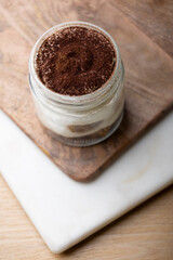 Delicious tiramisu dessert served in a glass jar, showcasing creamy layers of mascarpone cheese and coffee-soaked ladyfingers. Accompanied by a jar of extra ladyfingers