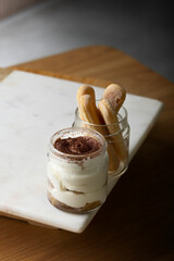 Delicious tiramisu dessert served in a glass jar, showcasing creamy layers of mascarpone cheese and coffee-soaked ladyfingers. Accompanied by a jar of extra ladyfingers