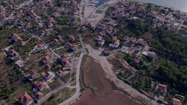 Aerial view of pink lake and town with coastal houses and trees, Zablace, Croatia.