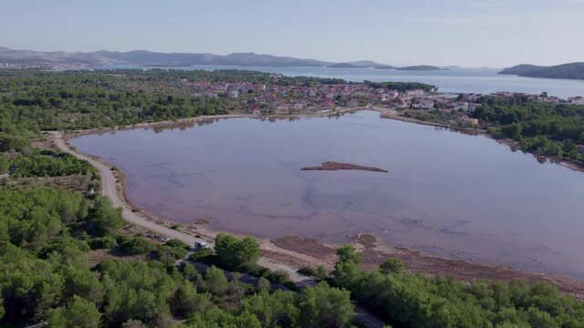 Aerial view of pink lake and town in forested mountains, Zablace, Croatia.