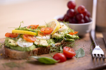 A delicious breakfast plate featuring poached eggs, avocado toast with lemon and tomato, a fresh salad, and a small bunch of grapes. Perfect for healthy eating and gourmet food themes.