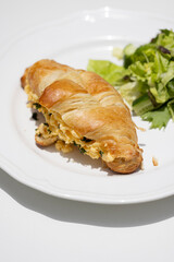 A breakfast spread featuring a croissant stuffed with scrambled eggs and herbs, served with a side salad on a white plate. Accompanied by a takeaway coffee cup from Postcard café,set on a wooden table
