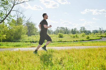 A male athlete is training on the sports ground outside. Caucasian male athlete jogging outdoors in a summer park