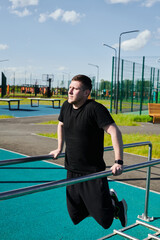 Fototapeta premium Caucasian male athlete doing pull-ups on the horizontal bar outdoors in a summer park