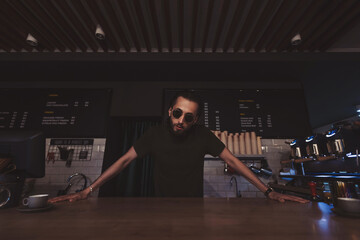Young cool barista with sunglasses standing behind the bar in cafe. small business