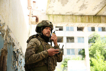 Military mission. Soldier in uniform with drone controller and radio transmitter near abandoned...