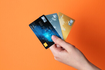 Woman holding credit cards on orange background, closeup