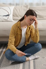 Obraz premium Sad woman holding pregnancy test on floor indoors