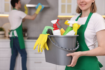 Cleaning service worker holding bucket with supplies in kitchen, closeup
