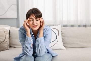 Upset woman suffering from headache on sofa at home